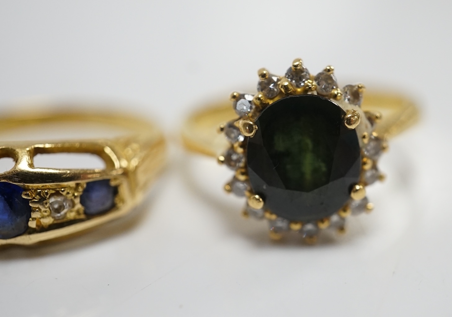 Two yellow metal and gem set rings, including a sapphire? and diamond oval cluster and a three stone sapphire and two stone diamond half hoop, gross weight 7.3 grams. Condition - poor to fair